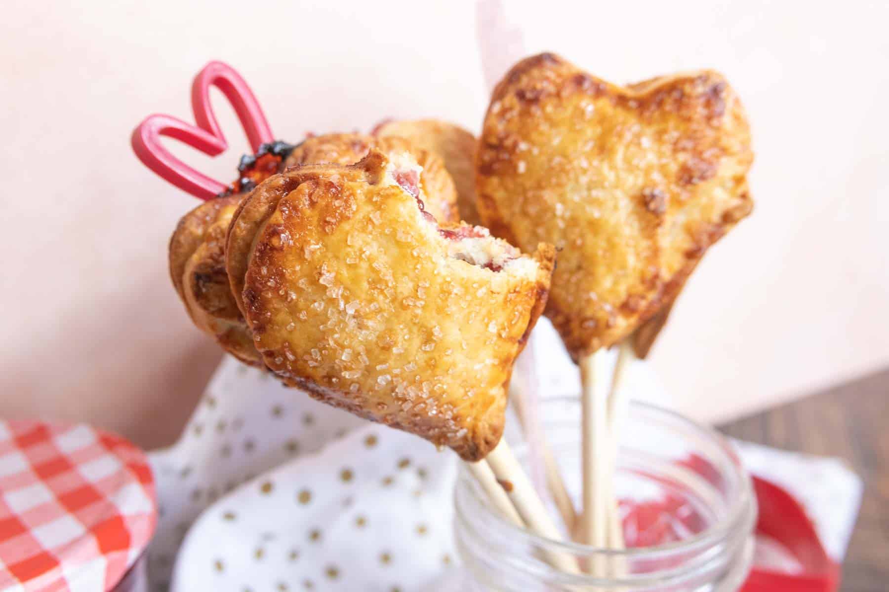 Heart-shaped pastries on sticks in a jar, with a decorative red ribbon detail.