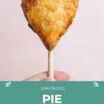 A hand holds a heart-shaped, golden-brown pie pop filled with jam on a stick against a light background. Text below reads "Jam-filled Pie Pops HappySnackcidents.com.