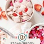 A bowl of strawberry Chex mix with pink, red, and white candy-coated chocolates sits among dried strawberries and extra candies. Text reads "Strawberry Chex Mix." Perfect for snacking or parties!.