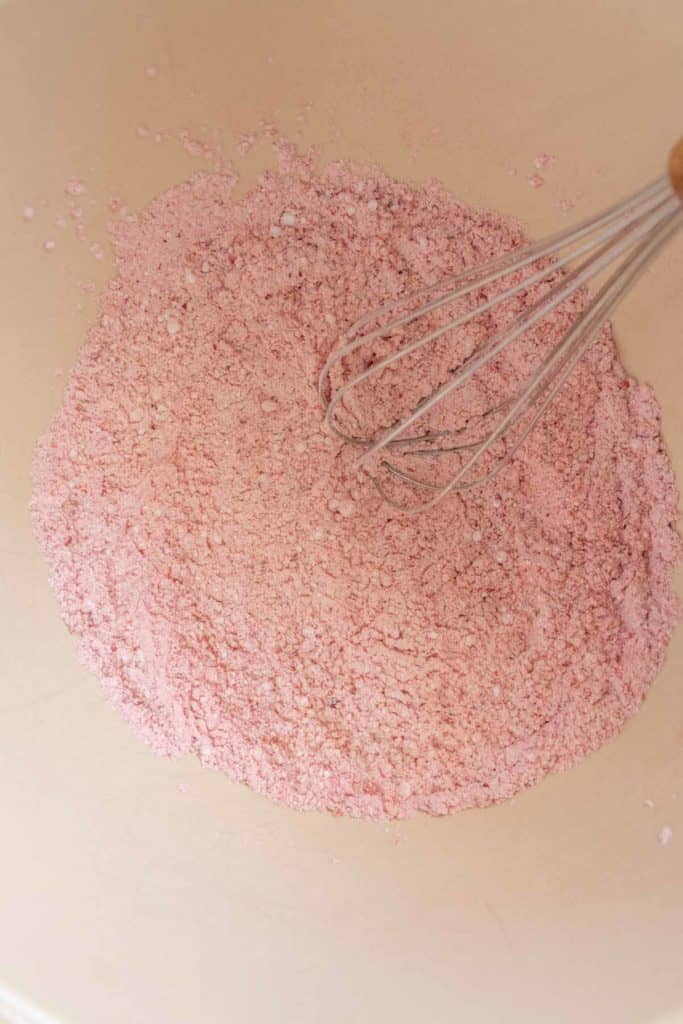 Whisk resting in a bowl of pink powdered mixture, possibly for baking.