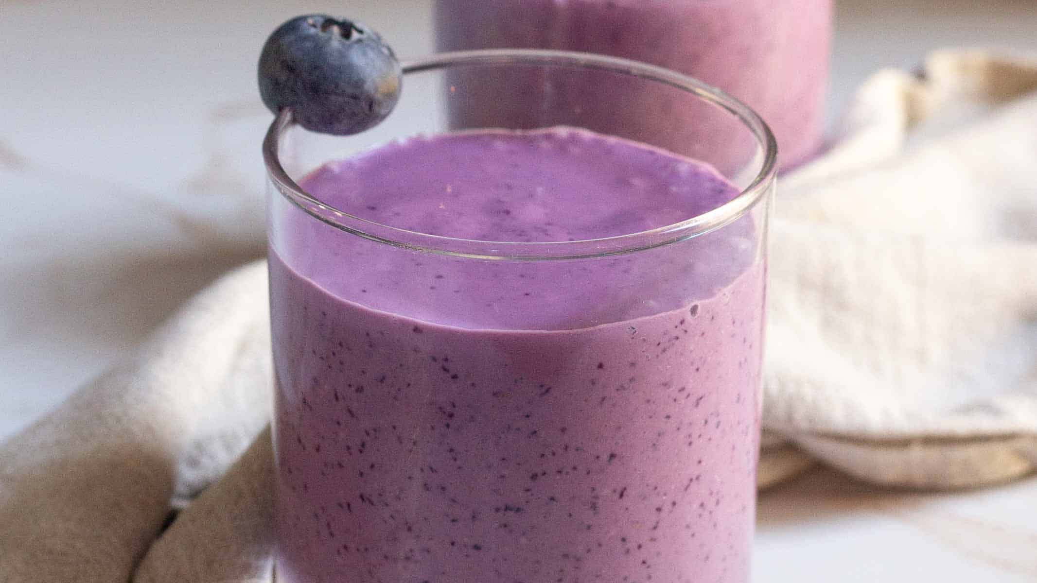 Thick blueberry smoothie in a glass, topped with fresh blueberry.