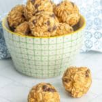 Bowl of oatmeal energy bites with chocolate chips on a tiled surface, with two bites placed outside the bowl.