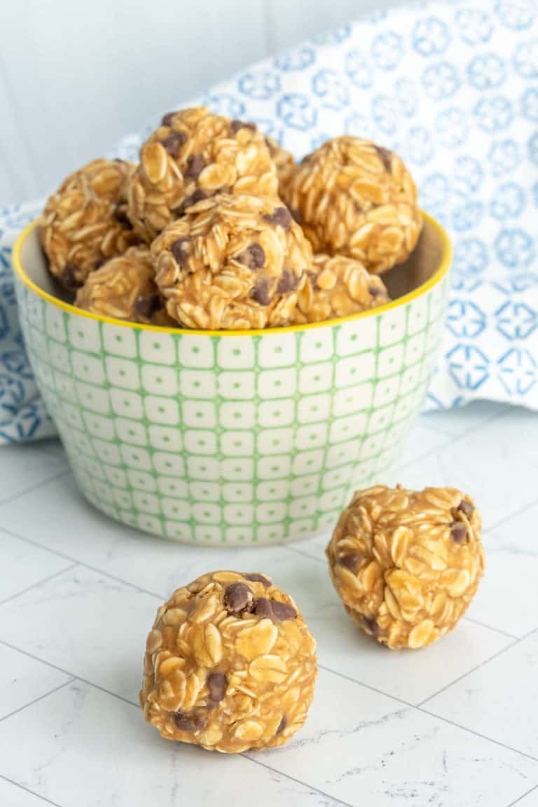 Bowl of oatmeal energy bites with chocolate chips on a tiled surface, with two bites placed outside the bowl.