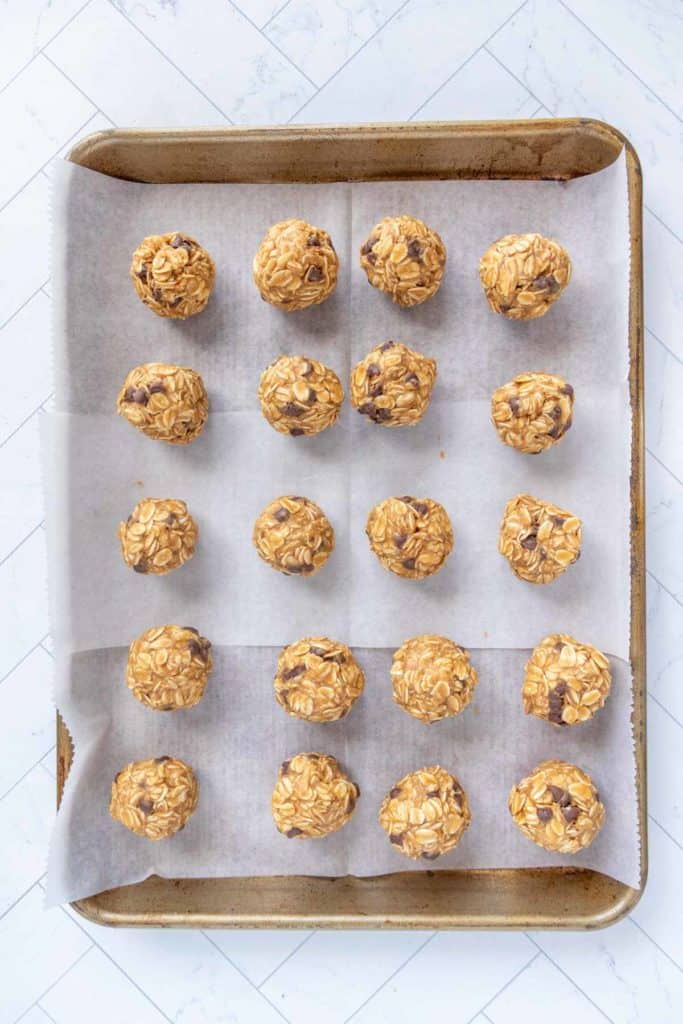 A baking tray with 20 oatmeal balls arranged in rows on parchment paper.