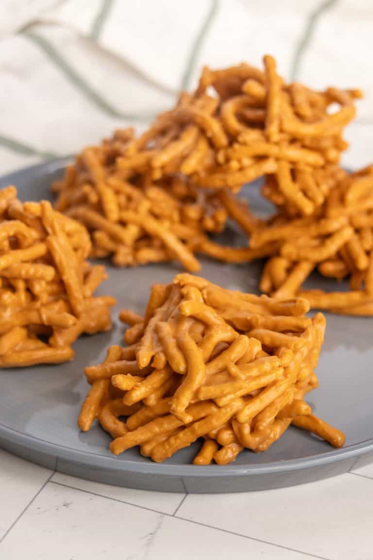 Clusters of butterscotch haystacks sit on a gray plate. They are made from thin, stick-like noodles coated in a golden butterscotch mixture.