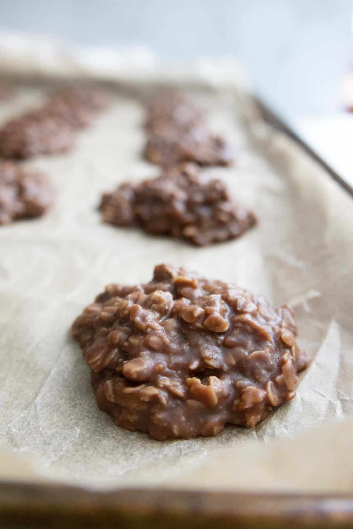 No-bake chocolate oatmeal cookies cooling on a parchment-lined baking sheet.