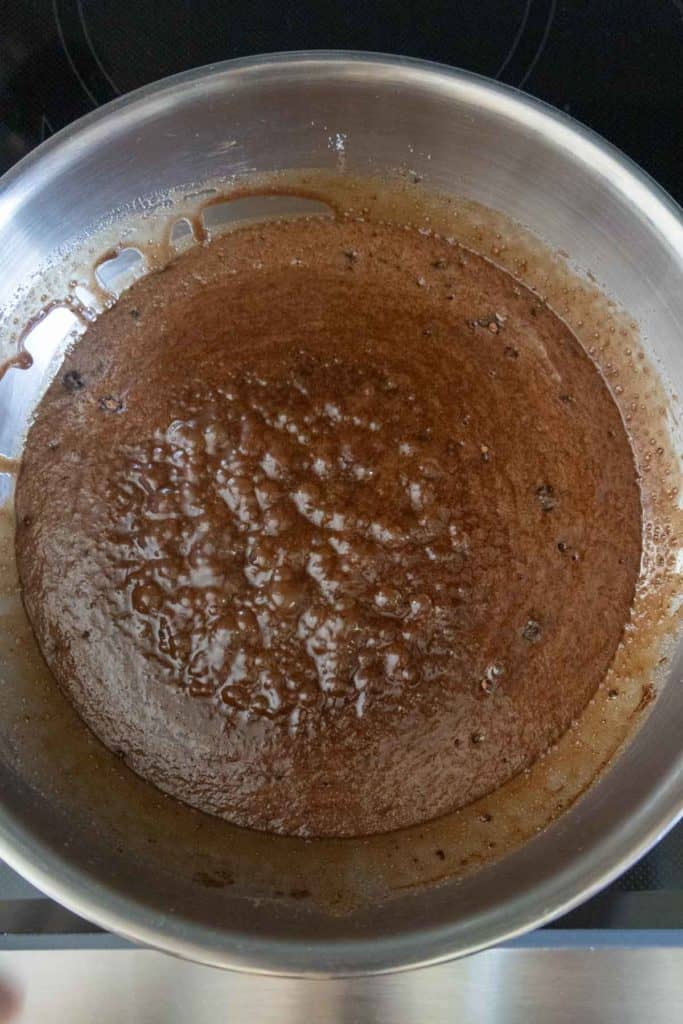 A stainless steel pan containing a layer of browned butter with dark brown bits and a glossy surface.