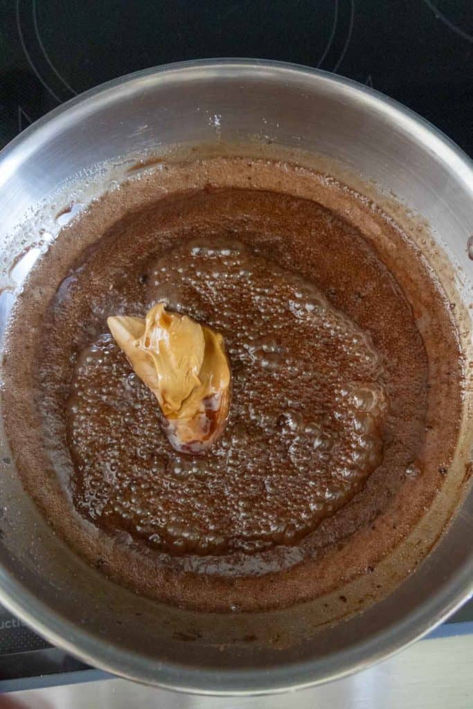 A saucepan containing melted chocolate with a dollop of peanut butter in the center, on a stovetop.