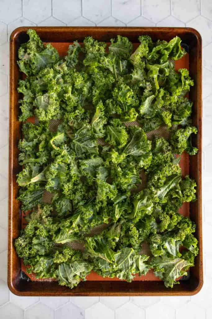 A baking sheet lined with parchment paper is covered with raw kale leaves, ready for roasting.
