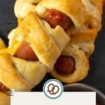 Close-up of crescent roll-wrapped hot dogs resembling mummies, served with a side of ketchup. A label at the bottom reads "Mummy Hot Dogs" and "happysnackcidents.com.