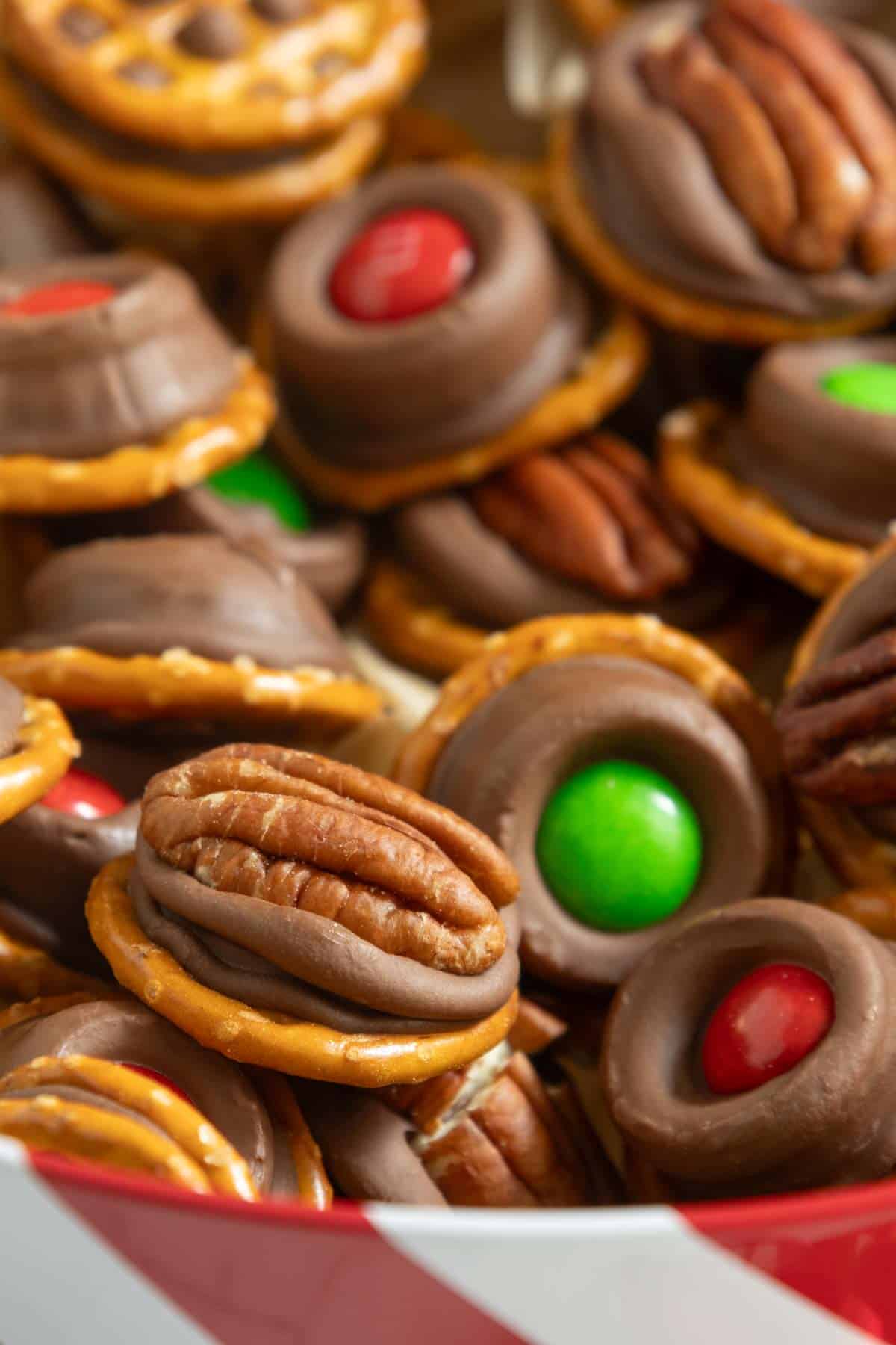 Close-up of pretzel treats topped with melted chocolate and either a pecan half or a red or green candy.