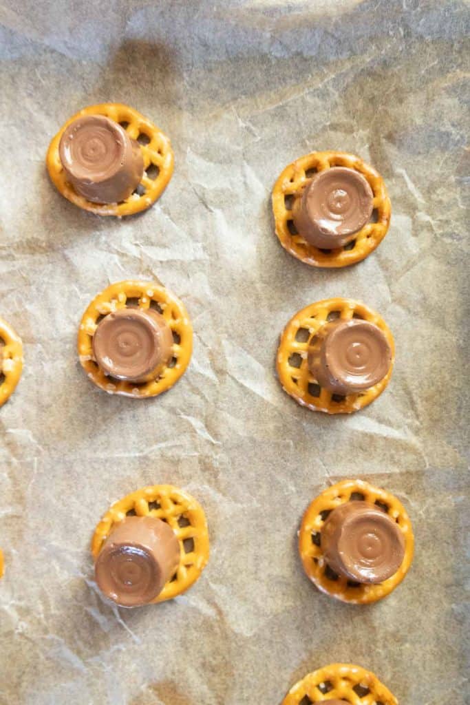 Round pretzels topped with chocolate-covered caramel candies are arranged on a sheet of parchment paper.