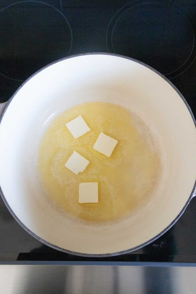 Four pieces of butter melting in a white pot on a stovetop.