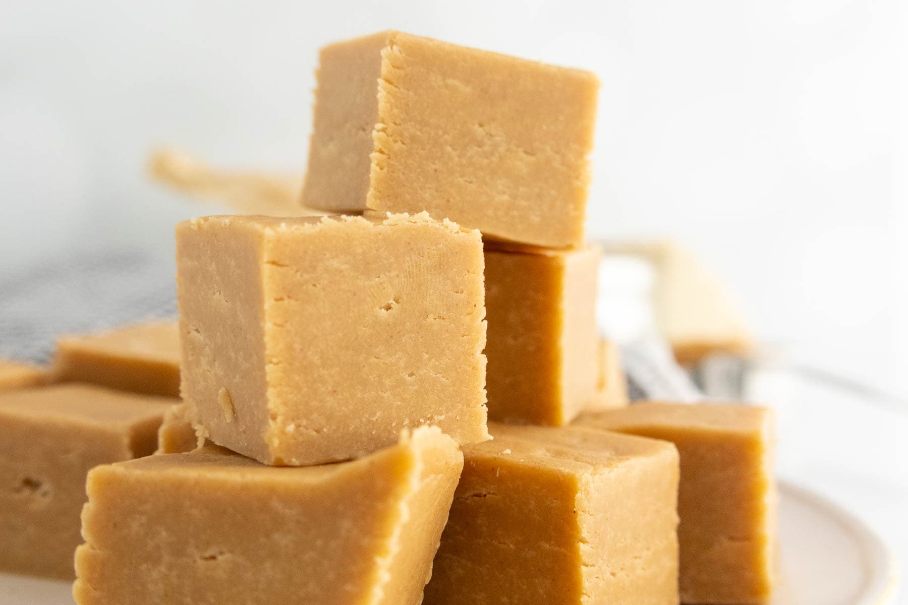 A close-up of several cubes of light brown fudge stacked on a white surface.
