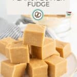 A plate with neatly stacked cubes of peanut butter fudge in front of a checkered cloth and bowl, with a label reading "Peanut Butter Fudge.