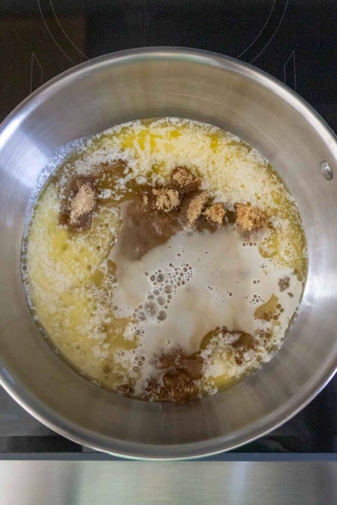 Melted butter, brown sugar, and milk are being combined in a stainless steel saucepan on a stovetop.