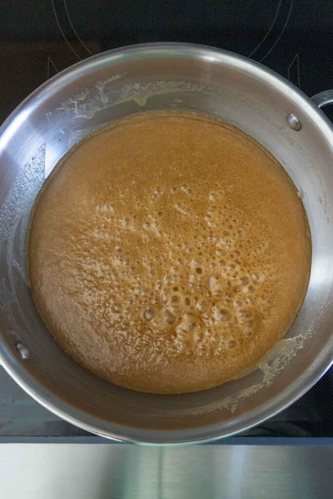 A saucepan on a stovetop containing a bubbling, caramel-colored mixture.