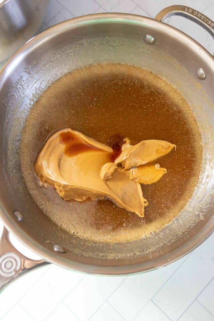 A metal pan containing melted butter, peanut butter, and a splash of vanilla extract, ready to be mixed together.