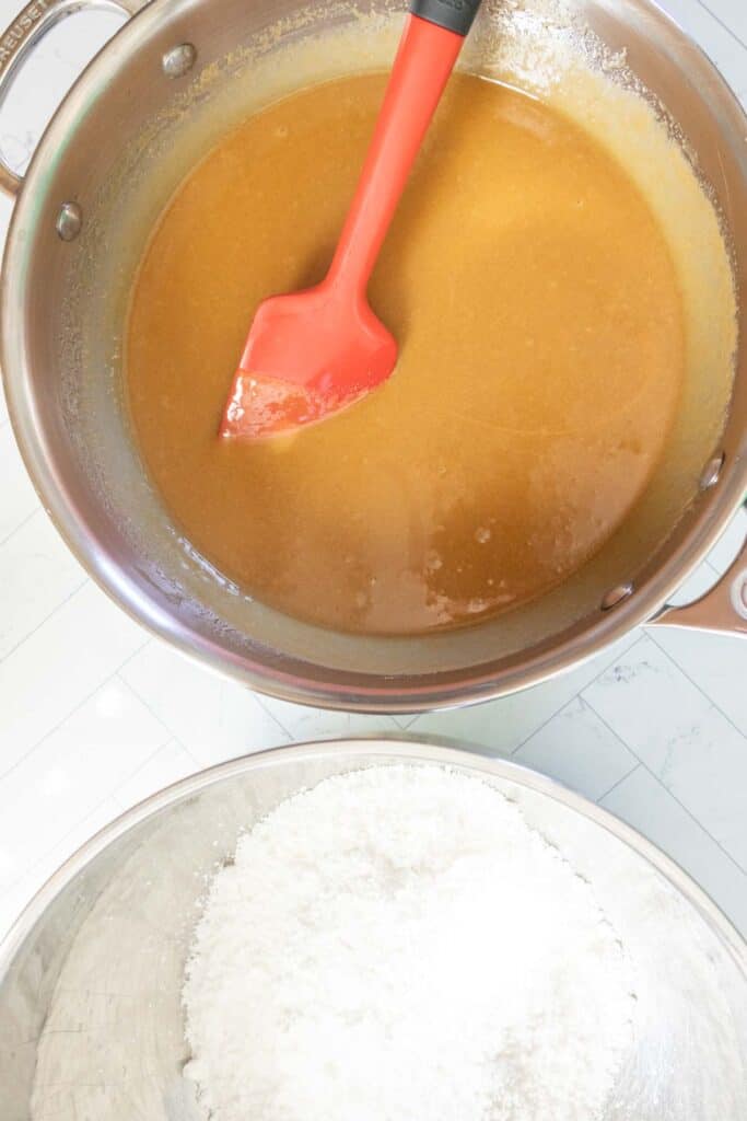 A bowl of brown batter with a red spatula and a separate bowl of white powdered ingredients on a white countertop.