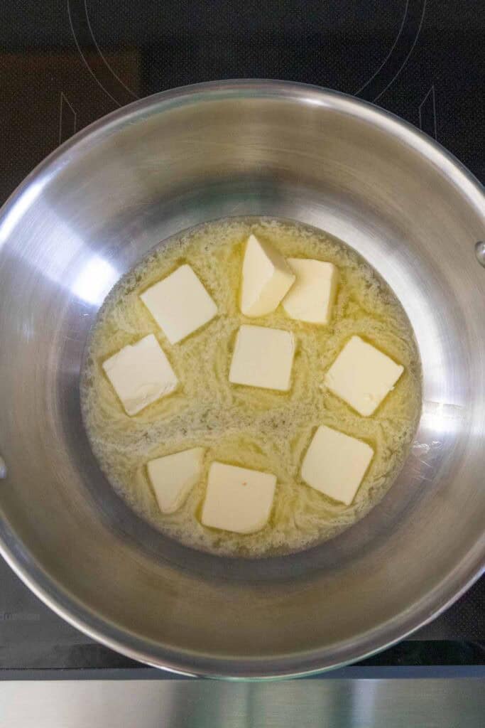 Sliced pieces of butter melting in a stainless steel pan on a stovetop.