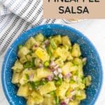 A blue bowl filled with pineapple salsa made with chopped pineapple, red onion, jalapeño, and cilantro, placed on a white surface with a striped towel nearby.