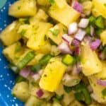 Close-up of pineapple salsa with diced pineapple, red onion, jalapeño, and cilantro in a blue bowl. Text on image reads: "Pineapple Salsa happysnackcidents.com".