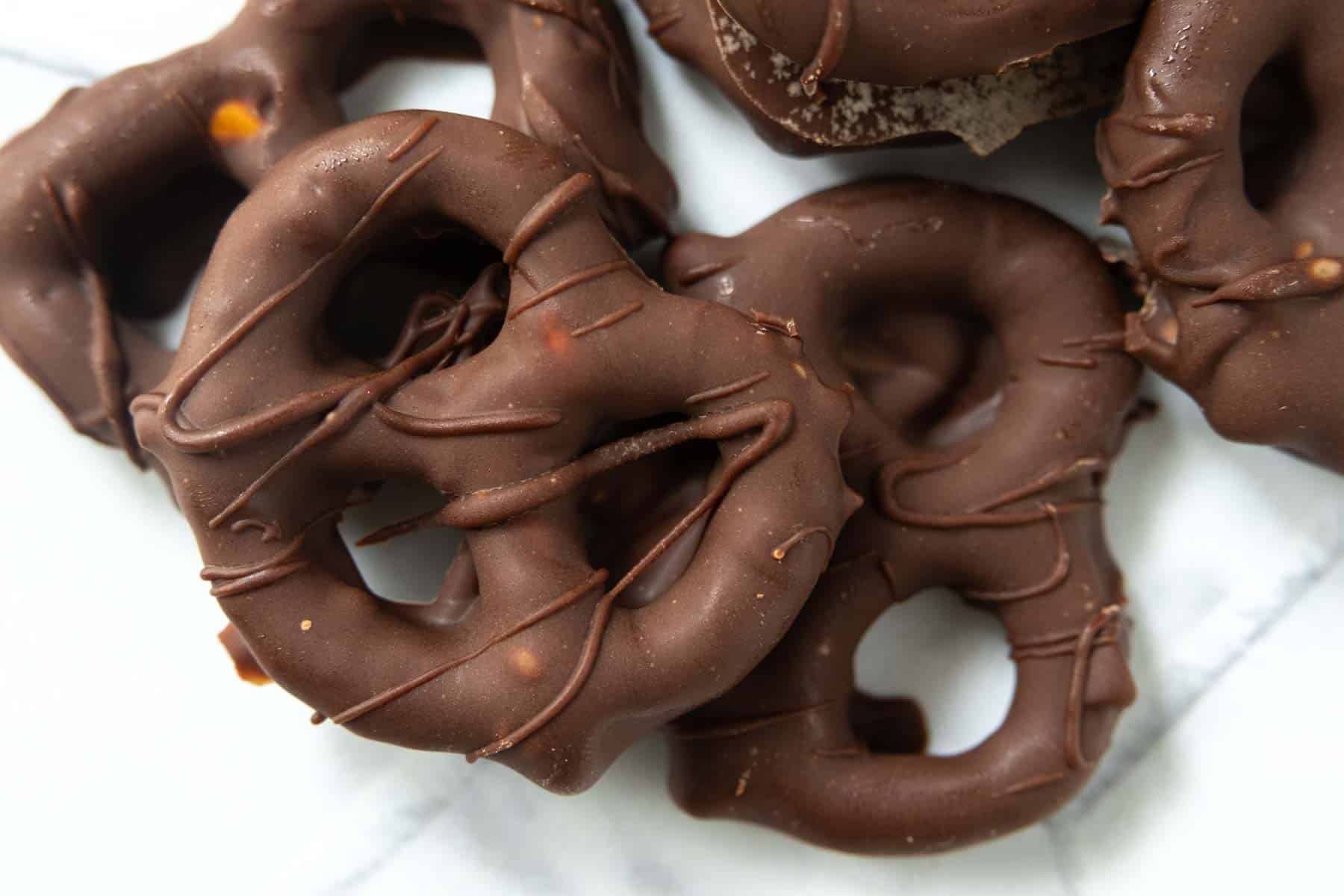 Chocolate-covered pretzels arranged on a white marble surface.