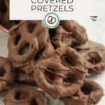 A pile of chocolate-covered pretzels on a white surface with a sign that reads “Chocolate Covered Pretzels” and a website URL at the bottom.