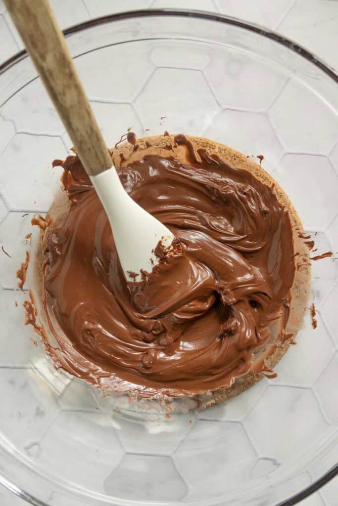 A mixing bowl with melted chocolate being stirred by a white spatula.