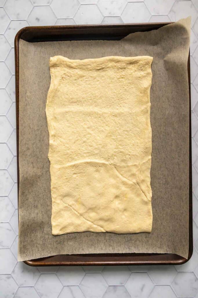 A sheet of raw dough is laid out on parchment paper on a baking sheet.
