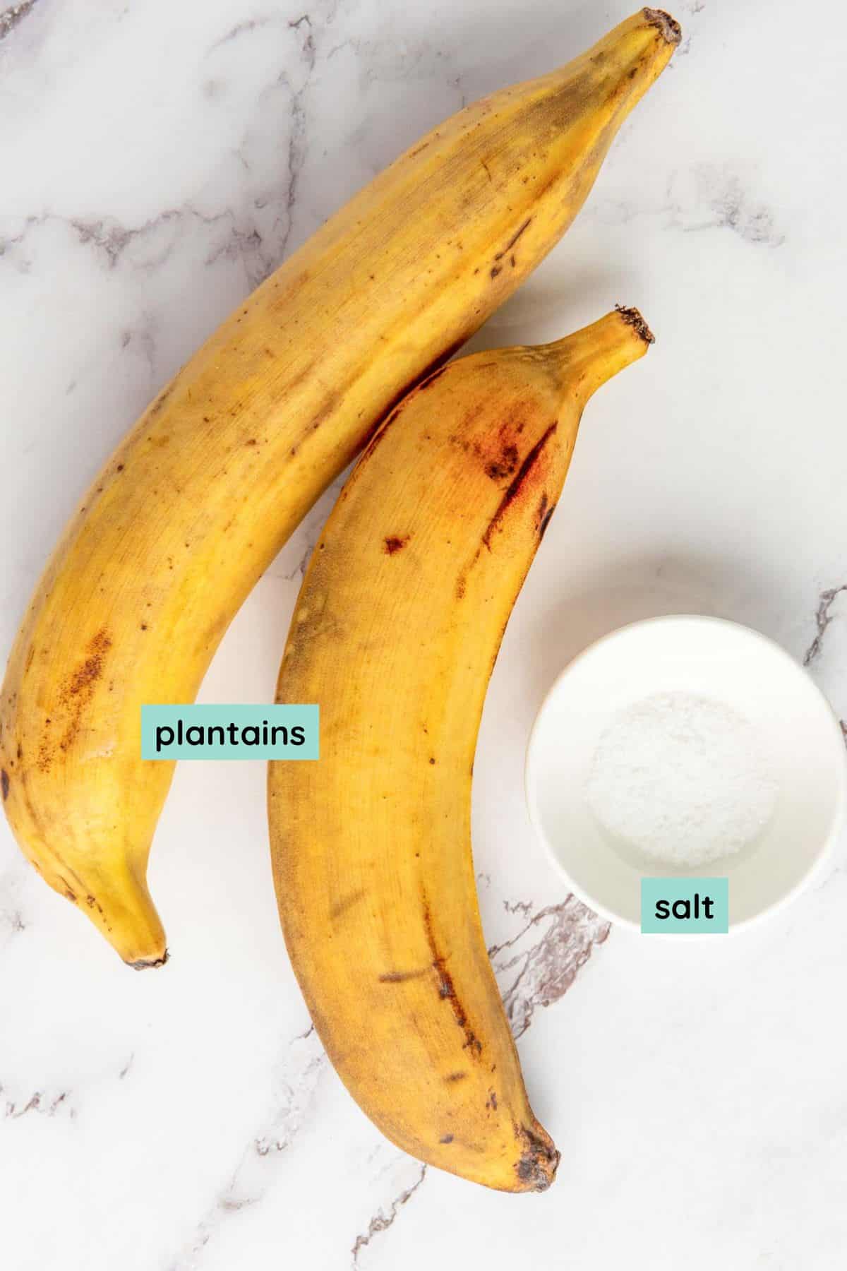 Two yellow plantains and a small white bowl of salt on a marble surface.