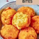 A bowl of golden-brown mac and cheese bites, one with a visible cheesy pasta filling, sits on a light surface.